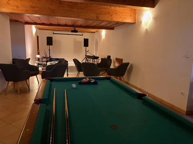 Kulečníkový stůl ve společné místnosti, za ním křesla a hudební nástroje.
