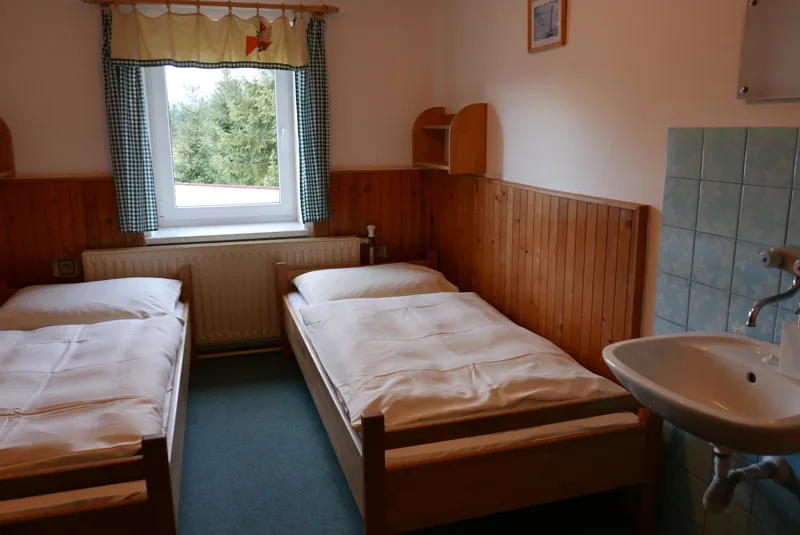 Dvě oddělené postele, okno a umyvadlo v pokoji