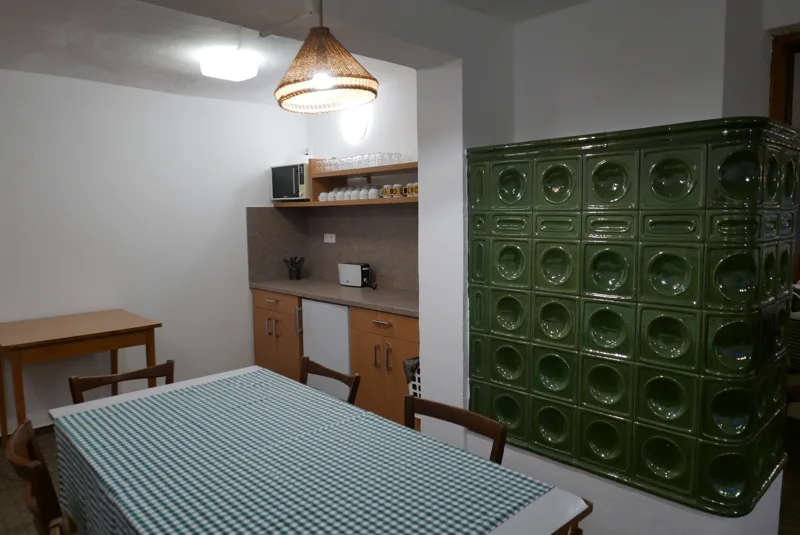Stůl a zelená kachlová kamna ve společné místnosti