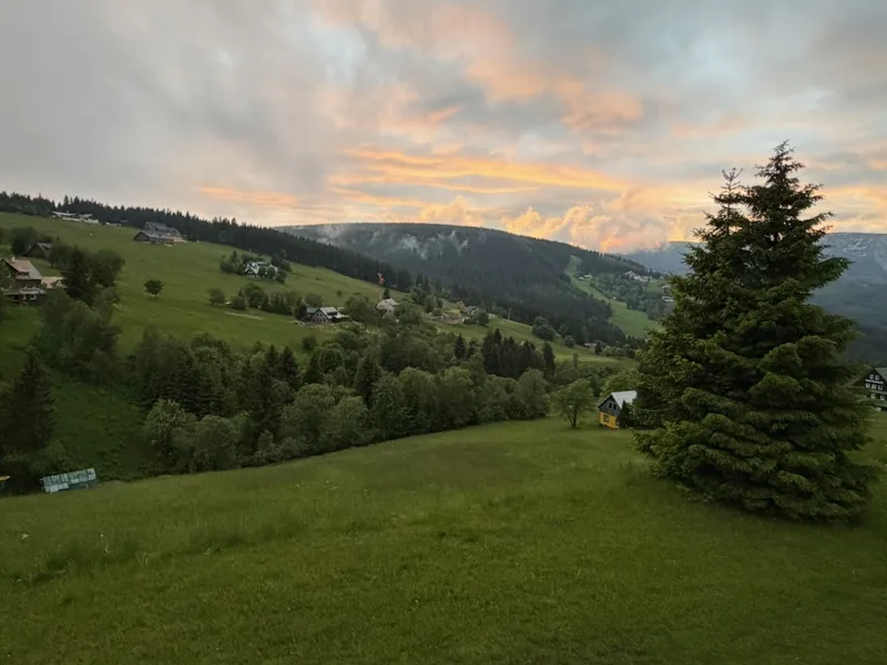 Zelené horské louky a chalupy pod večerní oblohou